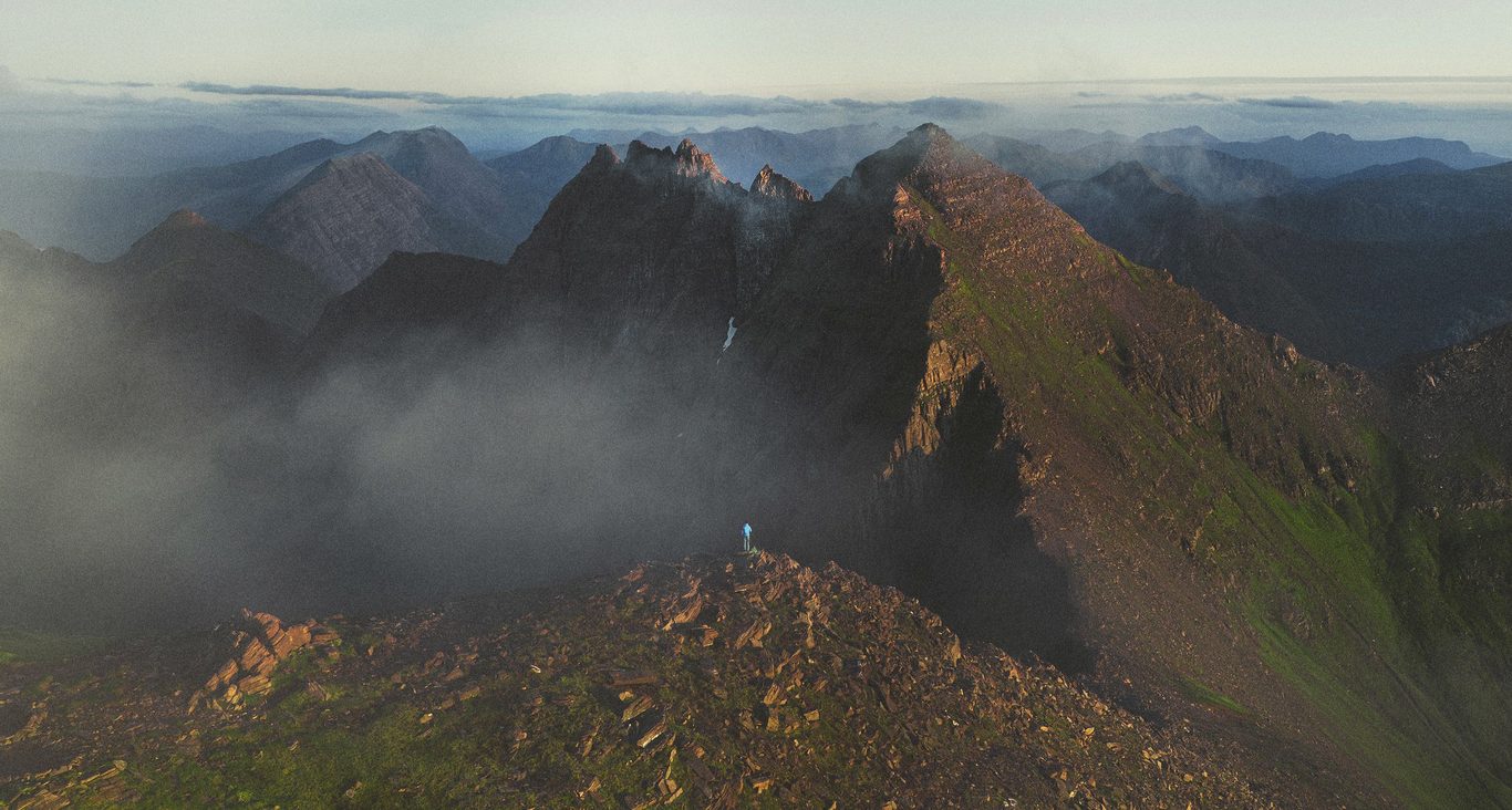 A lone hiker on a rocky summit above misty mountain ridges